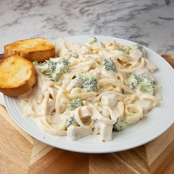 Creamy fettuccine Alfredo with chicken and broccoli florets, served with two pieces of toasted garlic bread.