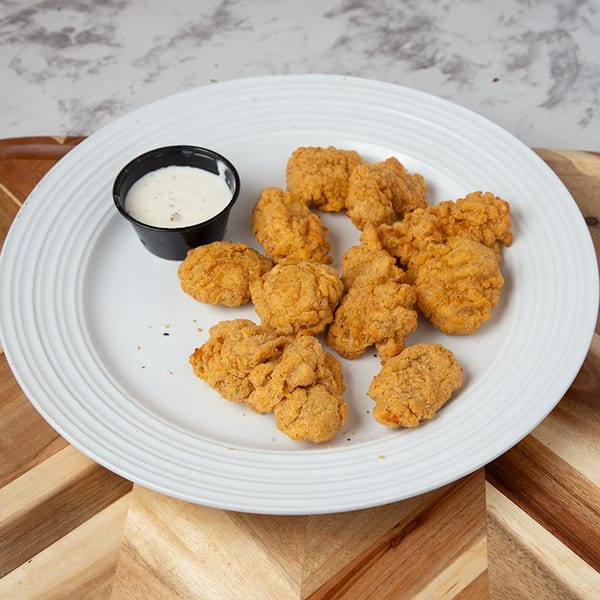Golden brown fried chicken nuggets with a side of ranch dressing on a white plate.
