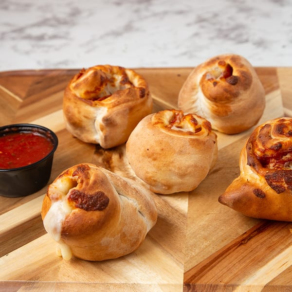 Five golden-brown pizza rolls with melted cheese and sauce, served with a side of marinara on a wooden board.