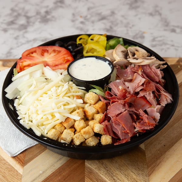 A large chef salad with ham, cheese, tomatoes, olives, peppers, mushrooms, croutons, and dressing.
