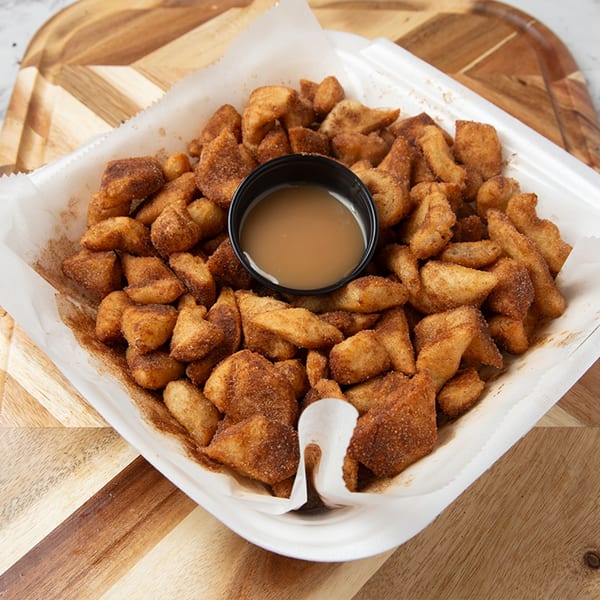 Cinnamon sugar knots from Tomatoes II Pizzeria, with a side of dipping sauce in a white container.